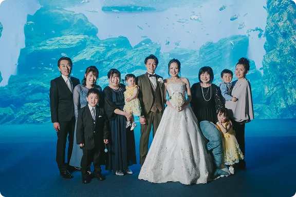 仙台うみの杜水族館でのウェディングフォト｜ドレス・タキシードの新郎新婦を囲むように両家の家族みんなでの集合写真
